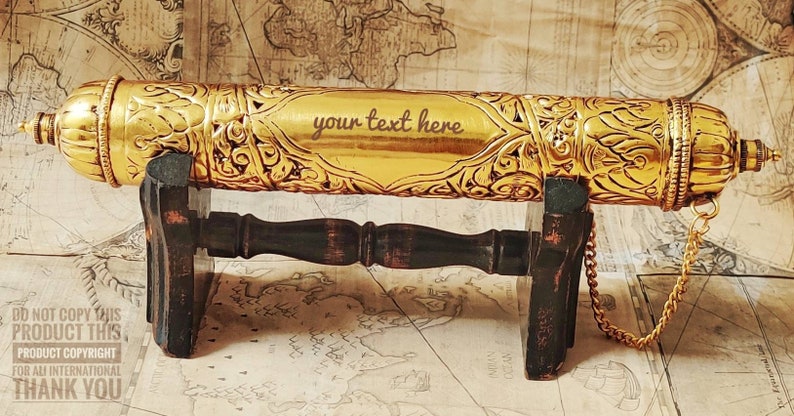 May include: A gold-colored decorative scroll tube with intricate floral designs. The tube is on a wooden stand and has a chain attached. The text "your text here" is engraved on the tube.