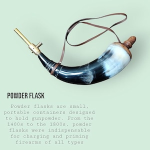 May include: A curved powder flask made from a polished black and white animal horn, featuring a brass nozzle, a wooden stopper at the base, and a thin brown leather carrying strap. The text POWDER FLASK is printed above a descriptive paragraph.