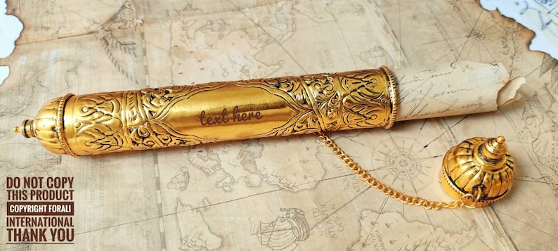 May include: A gold metal scroll tube with intricate designs and a chain attached. The tube is open and a rolled piece of paper is inside. The text "text here" is engraved on the tube.
