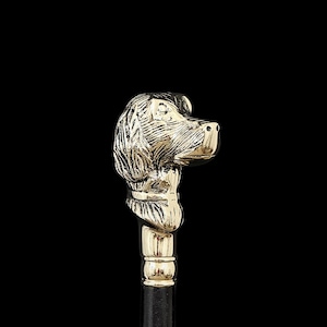 May include: A gold-colored dog head cane handle with a black shaft. The dog head is detailed with etched fur and facial features. The handle is a decorative accessory.