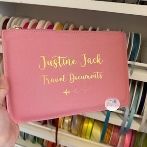 Pu&ograve; includere: Portadocumenti da viaggio rosa con cerniera dorata e il testo "Justine Jack Travel Documents" e due piccoli aerei con una linea tratteggiata tra loro. L'angolo in basso a destra ha un piccolo logo che dice "Georgina Ray Designs".