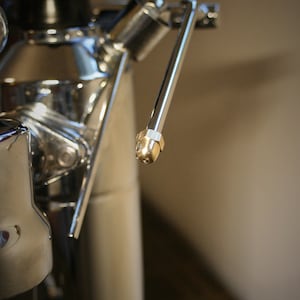 May include: Close-up of a silver espresso machine with a gold-colored steam wand.