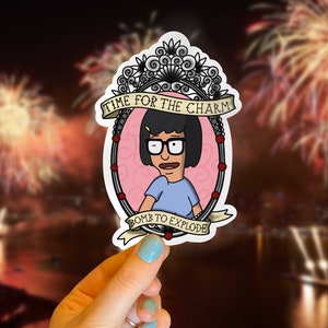 May include: A sticker featuring a cartoon character with glasses and a blue shirt, framed in a decorative oval. The sticker has the text "TIME FOR THE CHARM" and "BOMB TO EXPLODE" on banners.