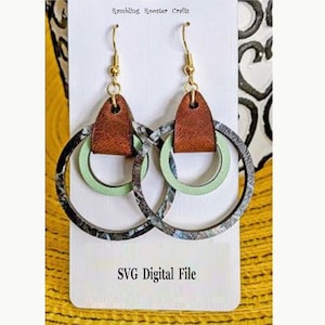 May include: A pair of dangle earrings with a brown leather accent and two layered circles. The outer circle is black and white with a marble pattern. The inner circle is a light green color. The earrings are displayed on a white card with the text "Rambling Rooster Crafts" and "SVG Digital File".