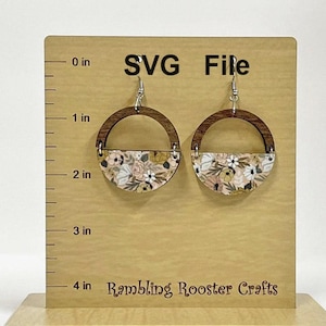 May include: A pair of wooden earrings with a floral pattern. The earrings are shaped like a half circle and have a silver hook. The earrings are displayed on a wooden board with a ruler.