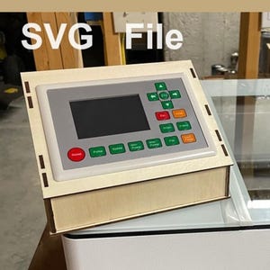 May include: A close-up of a laser cutter control panel with a small LCD screen and a variety of buttons. The panel is made of wood and has a light wood grain finish. The text "SVG File" is visible in the background.