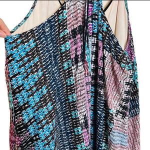 May include: A sleeveless dress with a geometric pattern in shades of blue, pink, and black. The dress has a V-neckline and a loose, flowing silhouette.