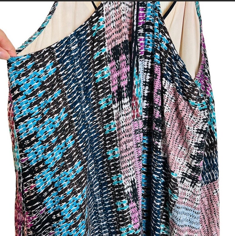 May include: A sleeveless dress with a geometric pattern in shades of blue, pink, and black. The dress has a V-neckline and a loose, flowing silhouette.