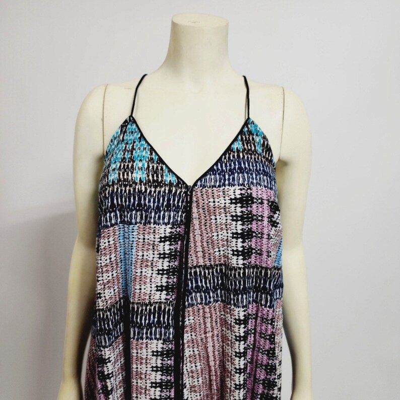 May include: A sleeveless top with a geometric pattern in shades of blue, pink, and black. The top has a V-neckline and thin black straps.