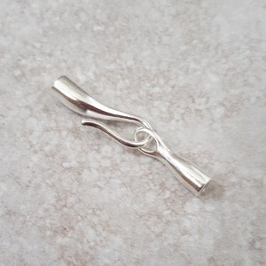 May include: A silver jewellery clasp with a curved design. The clasp has a hook and eye closure, and is made of a shiny, metallic material. The clasp is designed for necklaces, bracelets, or other jewellery items.