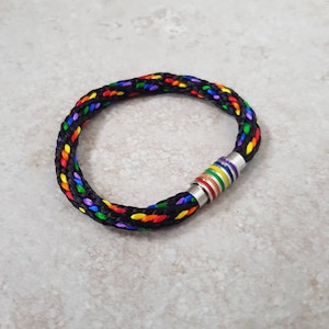 May include: A black braided bracelet with a rainbow coloured stripe and a silver magnetic clasp.