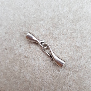 May include: Silver metal clasp with a unique design, featuring a curved shape and a loop. This clasp is ideal for jewellery making or other craft projects.