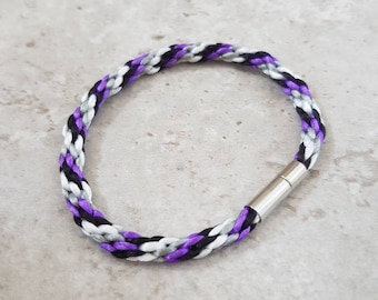 May include: A braided bracelet with purple, black, and white threads. The bracelet has a magnetic clasp.