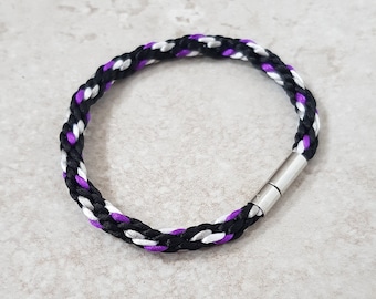 May include: A braided bracelet with black, white, and purple cord, featuring a silver magnetic clasp.