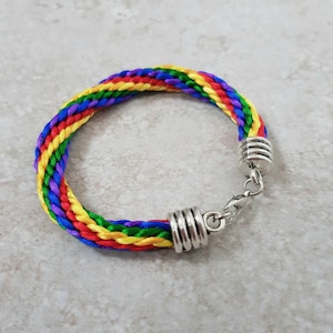 Puede incluir: Un brazalete trenzado de colores arcoíris con cierres y tapas de metal plateado.