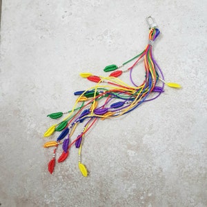 May include: A rainbow-colored keychain with a silver clasp and multiple strands of string with small, colorful leaf-shaped beads.