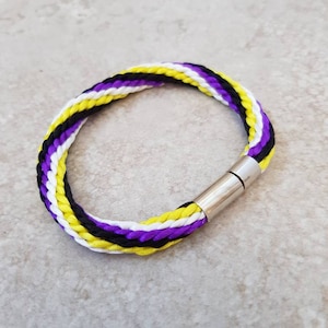 May include: A braided bracelet with yellow, white and purple stripes and a silver magnetic clasp.