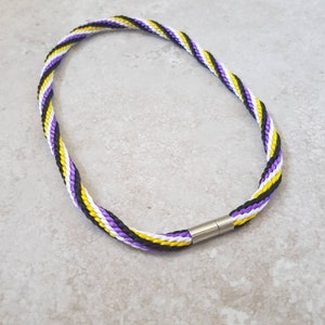 Könnte beinhalten: Ein lila, weißes und schwarzes Lanyard mit einem silbernen Verschluss. Das Lanyard besteht aus geflochtener Schnur.