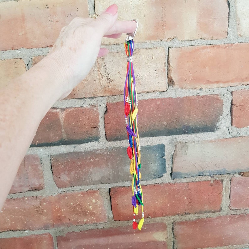 May include: A colorful keychain with a silver clip and multiple strands of yarn in red, yellow, green, blue, and purple. Small red, yellow, and purple beads are attached to the strands.