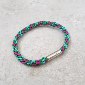May include: A braided bracelet with green, blue and pink threads. The bracelet has a magnetic clasp.