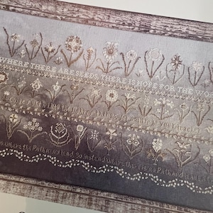 May include: A framed embroidery with floral motifs and inspirational text. The design features rows of stylized flowers in shades of brown and white against a gradient gray background. The text reads, "WHERE THERE ARE SEEDS, THERE IS HOPE FOR THE WORLD."