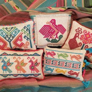May include: Five embroidered throw pillows with colorful geometric patterns and designs. The pillows are made of a natural linen fabric and have a fringe trim. The designs include birds, flowers, and abstract shapes.