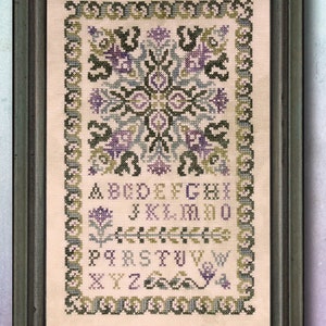 May include: A cross-stitch sampler with a floral design in the center and the alphabet in a border around the outside. The design is stitched in shades of green, purple, and blue on a cream-colored fabric.