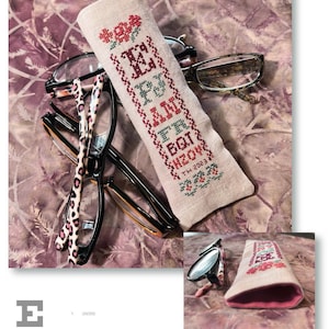 May include: A beige linen eyeglass case with pink stitching and embroidered with the text "I pray I got this" and the date "11th 2023". The case is lying on a purple and brown patterned fabric with three pairs of eyeglasses on top of it.