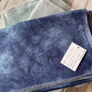 May include: A blue linen fabric with a white tie-dye pattern. The fabric is folded and has a label with the name "Sunken Depths" and the following information: Alda: 14 16 18 20, Lugana: 28 32, Linen: 28 32 36 40 46 56, www.lapinloops.com