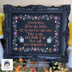 May include: A black framed cross-stitch with a white background and colorful floral border. The cross-stitch features a poem that reads: "Crosspatch, Draw the latch. Sit by the fire and spin. Take a cup, And drink it up. Then call your neighbors in."