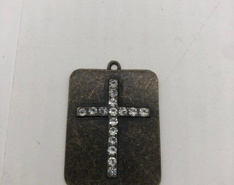 May include: A rectangular pendant with a cross design. The pendant has a bronze-colored finish with a textured surface. The cross is adorned with clear, sparkling rhinestones, adding a touch of elegance to the religious symbol.