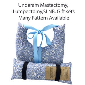 Puede incluir: Una almohada de mastectomía con estampado floral azul y una almohada a juego con una correa negra. La parte superior de la almohada tiene una cinta azul atada con un lazo. El texto de la imagen dice: Underam Mastectomy, Lumpectomy, SLNB, Gift sets, Many Pattern Available.