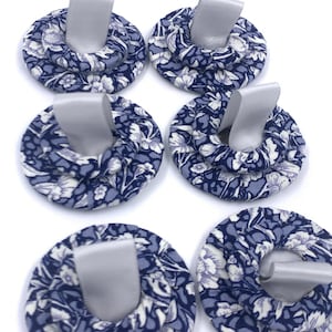 May include: Six blue and white floral fabric circles with a silver ribbon loop. The circles are layered and have a 3D effect.