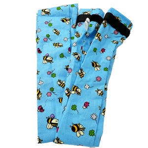 May include: Light blue leggings with a repeating pattern of cartoon bees, flowers, and ladybugs. The leggings have a black elastic waistband. The fabric is a soft, lightweight material.