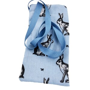May include: A pale blue fabric pouch featuring a repeating pattern of hares in black and white, with small insect motifs. It has a blue ribbon drawstring. The fabric has a textured finish.