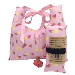 May include: Pink medical port comfort pillows with a watermelon and lemon pattern. The pillows have a pink ribbon and a black strap. The text on the label says "Medical Port Comfort Pillows" and "Make Seatbelts more bearable!"
