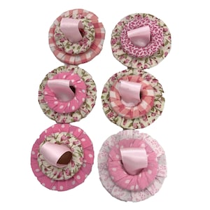 May include: Six handmade fabric flower embellishments in pink, white, and floral patterns. Each flower has a layered design with a satin ribbon centre. The flowers are arranged on a white background.