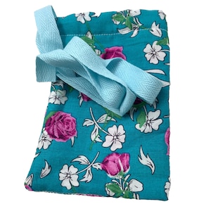 May include: A small turquoise drawstring bag with a floral print featuring pink roses and white flowers. The bag has a light blue drawstring.