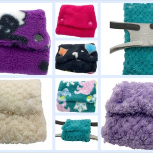 Puede incluir: Una colección de seis diferentes cubiertas de pañales de tela. Las cubiertas están hechas de varios colores y patrones, incluyendo morado con huellas de patas negras, rosa, turquesa, blanco, verde con flores rosas y azules, y morado.