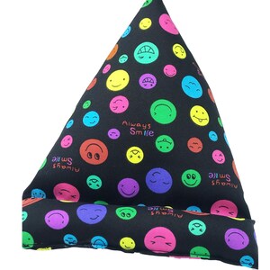 Puede incluir: Almohada triangular negra con un patrón de caritas sonrientes de colores. La almohada tiene el texto "Always Smile" impreso.