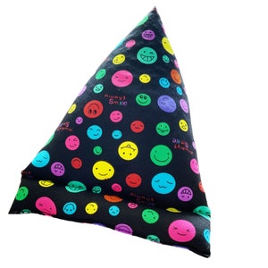 Puede incluir: Una almohada triangular negra con un colorido patrón de caras sonrientes. La almohada presenta varios emojis en tonos rosa, amarillo, verde, azul y morado. Las palabras "Always Smile" están impresas en la almohada.