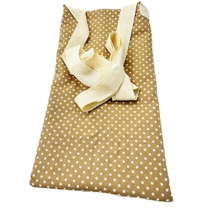 Puede incluir: Un bolso tote marrón con lunares blancos. El bolso tiene una correa de color crema que está doblada sobre la parte superior. El bolso está hecho de tela y está diseñado para llevarse al hombro.