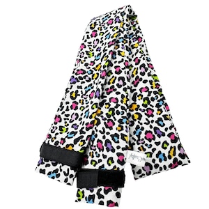 May include: A white fabric item with a colorful leopard print in black, pink, yellow, blue, and purple. The item has two black velcro straps and a small white tag that says "me Crafty!".
