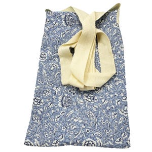 Könnte beinhalten: Eine blaue Tragetasche mit einem Blumenmuster in Weiß und Marineblau. Die Tasche hat einen cremefarbenen Riemen, der über die Oberseite gefaltet ist. Die Tasche ist aus Stoff und zum Tragen von Gegenständen bestimmt.