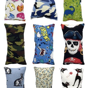 May include: A collection of nine rectangular pillows with various patterns. Designs include cats, camouflage, dinosaurs, comic book graphics, a pirate skull, rabbits, floral prints, and black cats. Each pillow has a black tag.