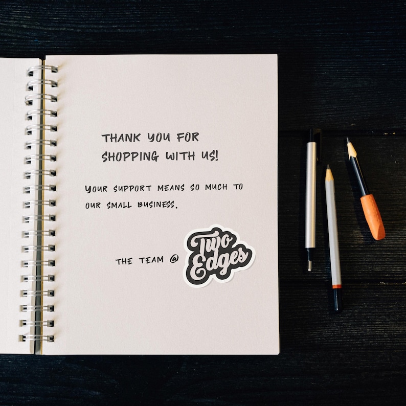 May include: A handwritten thank you note on a white spiral notebook with the text "THANK YOU FOR SHOPPING WITH US! YOUR SUPPORT MEANS SO MUCH TO OUR SMALL BUSINESS. THE TEAM @ Two Edges".