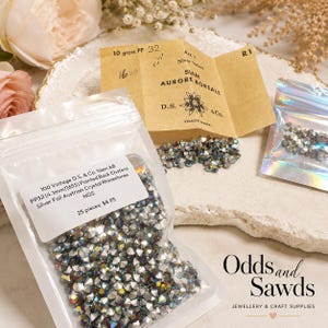 Puede incluir: Una bolsa de plástico transparente llena de pequeños cristales chatón de reverso puntiagudo con acabado iridiscente. Una etiqueta blanca dice 100 Vintage D.S. & Co. Siam AB PP32 (4,1 mm) 16SS Pointed Back Chatons Silver Foil Austrian Crystal Rhinestones NOS.