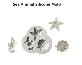 May include: A white silicone mold with three sea animal shapes: a starfish, a seashell, and a seahorse. The mold is shown with three finished sea animal shapes made of white material with blue glitter accents.