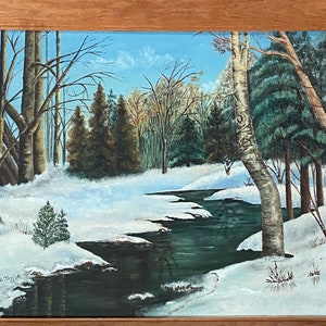 May include: A framed painting of a winter scene with a winding stream flowing through a snowy forest. The trees are bare and the ground is covered in snow. The painting is in a wooden frame.
