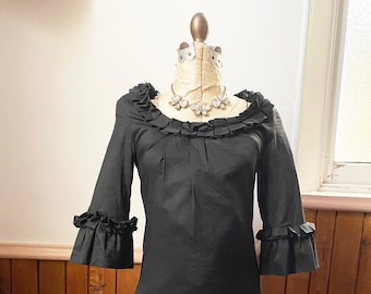 May include: A black dress with a ruffled neckline and sleeves. The dress has a fitted bodice and a flared skirt with multiple layers of ruffles.
